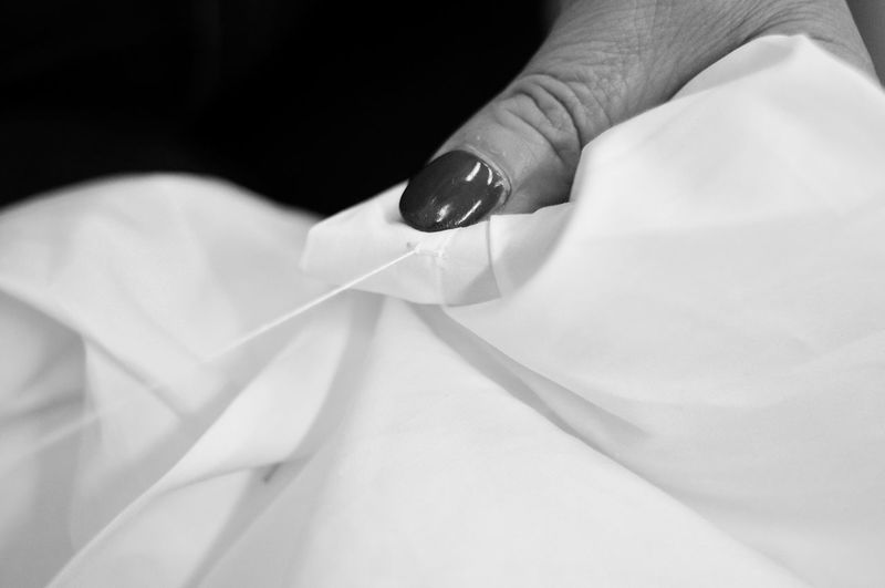 Cropped hand of woman sewing textile against black background
