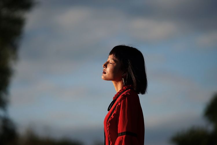 Side view of young woman standing against sky