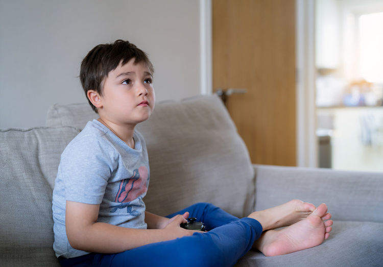 Boy looking away while sitting on sofa at home