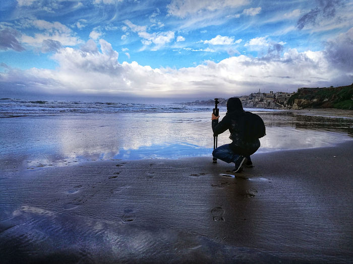 Man photographing at beach against sky