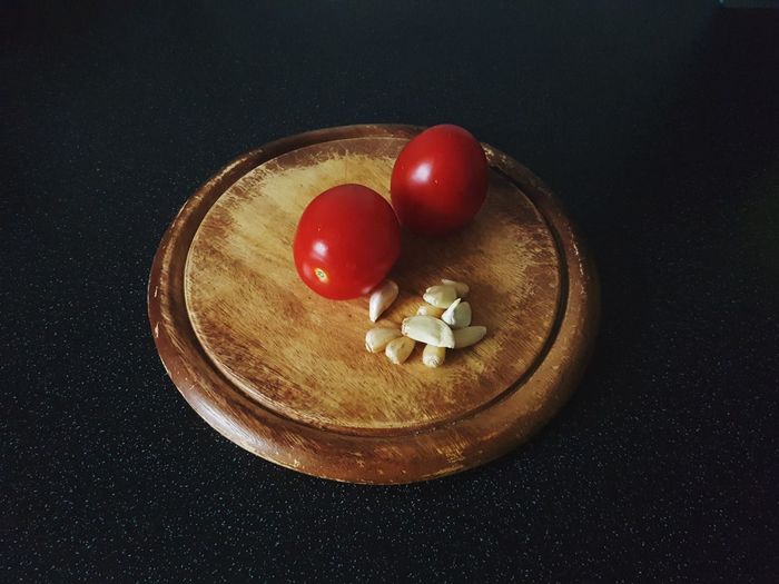 Close-up of tomatoes with garlic bulb with cutting board on table