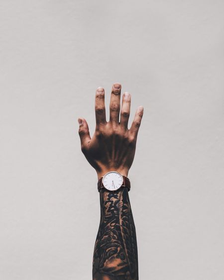 Cropped image of man hand with tattoo wearing wrist watch against white background