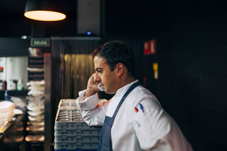 Side view of man working in restaurant kitchen and having phone call