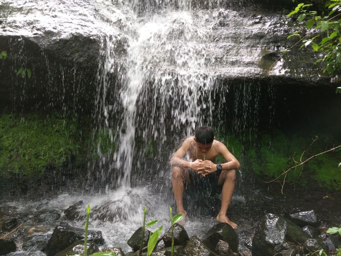 Full length of shirtless man splashing water in rocks