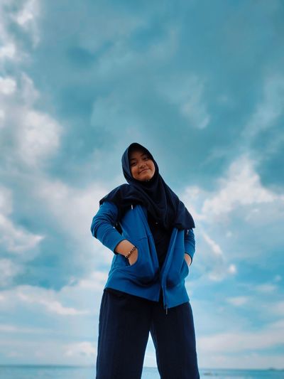 Low angle portrait of woman wearing hijab standing against cloudy sky