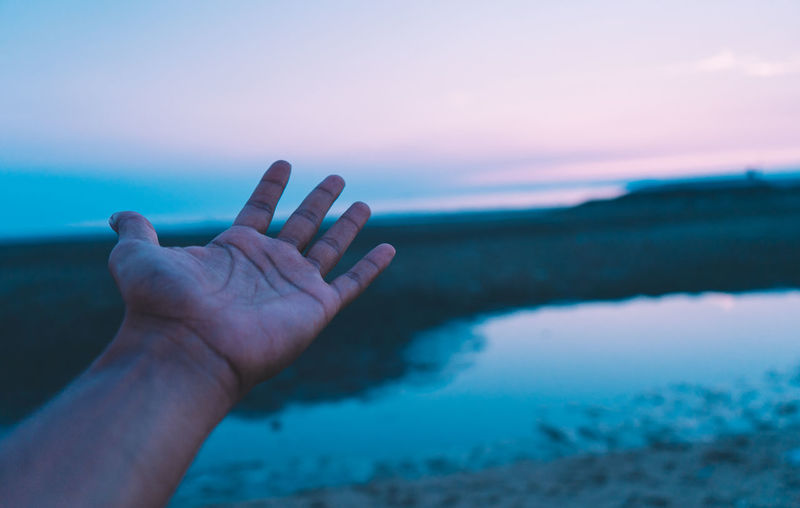 Close-up of hand against sea at sunset