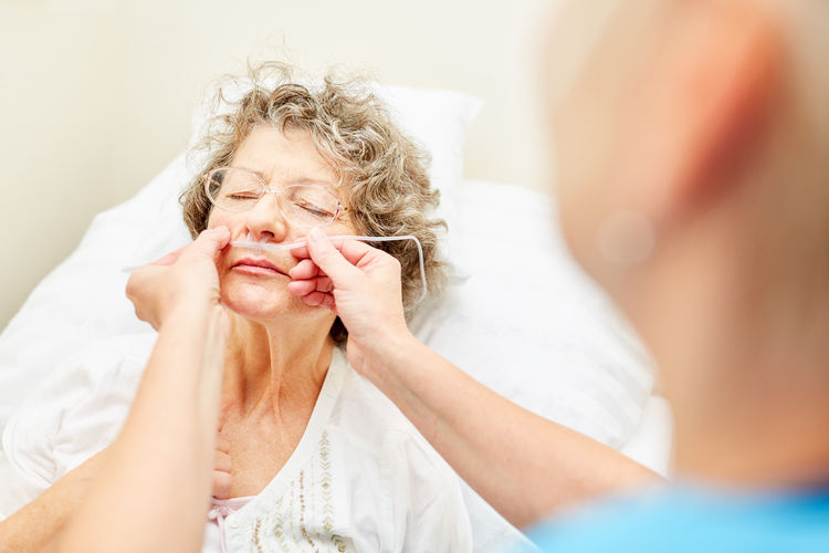 Nurse inserting oxygen tube in senior patient