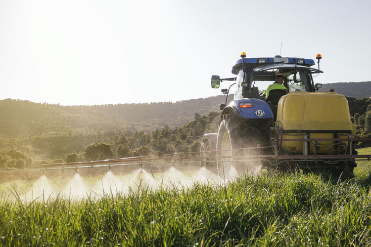 Young farmer spraying fertilizer through sprayer on tractor on field