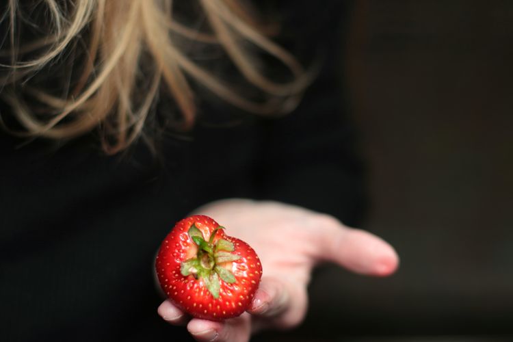 Close-up of hand holding strawberry against black background