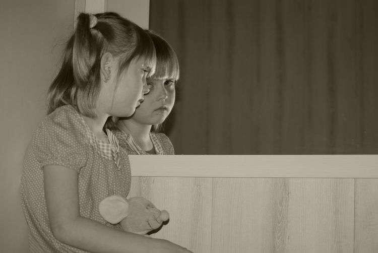 Girl holding stuffed toy looking at mirror reflection