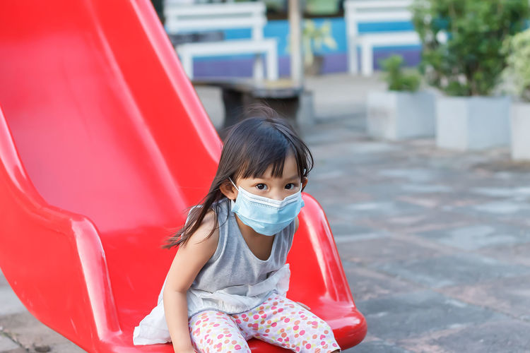 Portrait of cute girl wearing mask sitting on slide