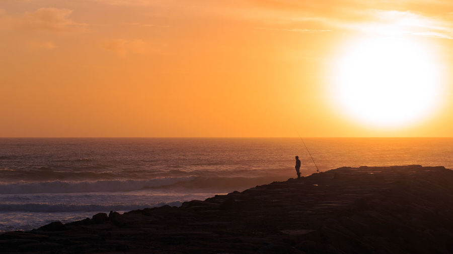 Scenic view of fisherman on pier at sunset