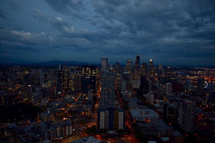 Aerial view of city lit up against cloudy sky