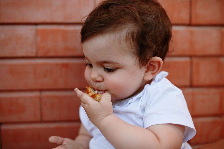 Cute boy eating food against wall