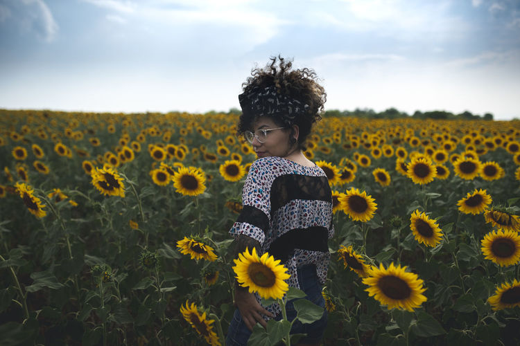 Side view of woman standing amidst sunflowers on field against sky