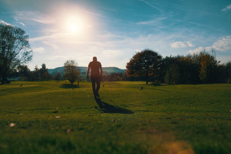 Rear view of man walking on golf course against sky