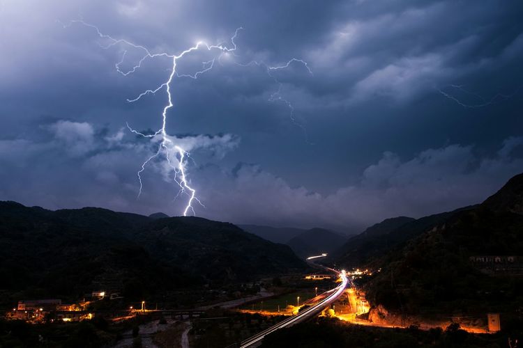 Scenic view of lightning over mountain by illuminated city