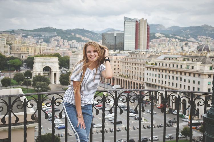 Portrait of smiling teenage girl standing against railing in city