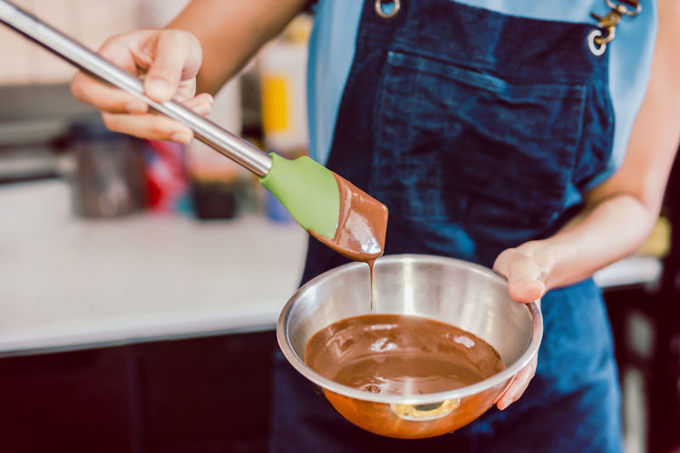 Woman mixing smooth delicious dark chocolate ganache with whisk in silver bow