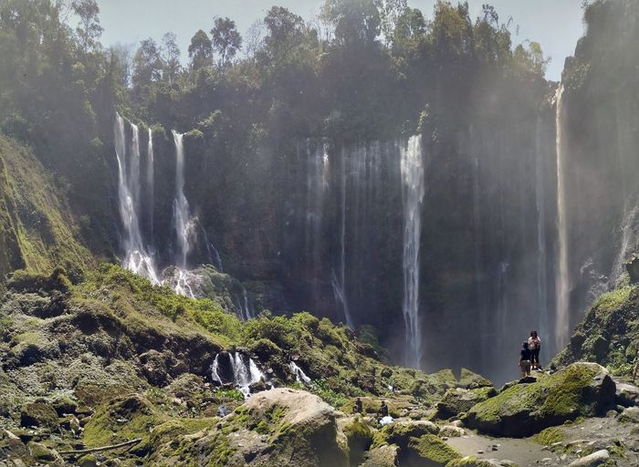 People standing on rock against waterfall
