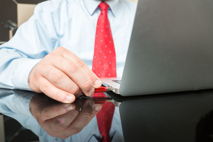 Midsection of businessman attaching usb stick to laptop at desk in office