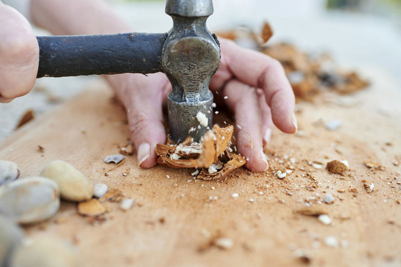 Hands of woman breaking almond husks with hammer