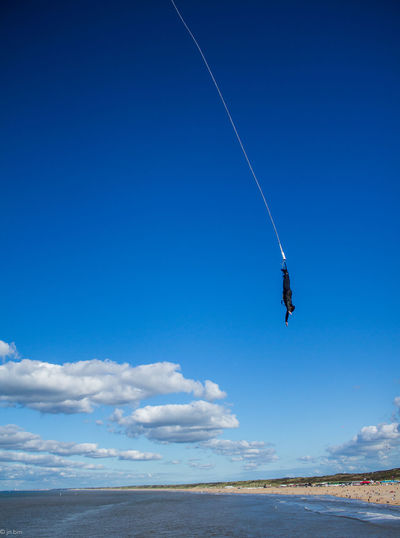 Person performing bungee jump against blue sky