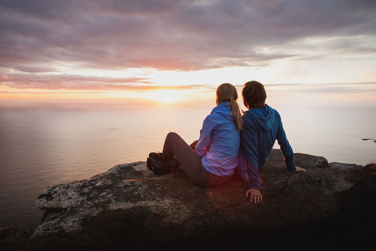 Rear view of couple looking at sea against sky during sunset