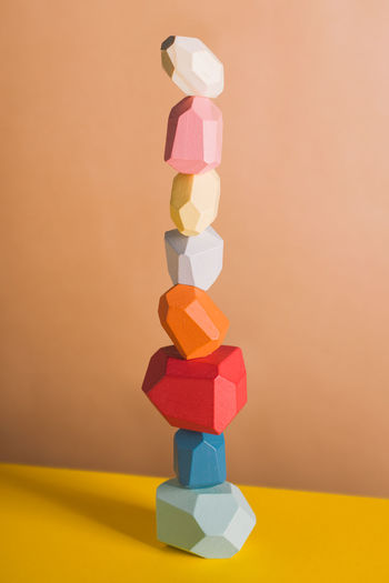 Wooden blocks in shapes of gems of various colors stacked on beige background in studio