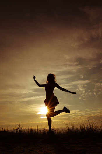 Silhouette woman with arms raised on field against sky during sunset