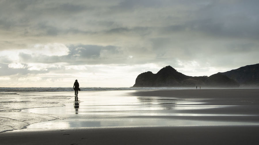 Silhouette man walking on beach against sky