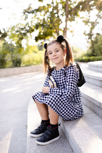Cute young child girl 5-6 year old wear checkered black and white dress and backpack holding books