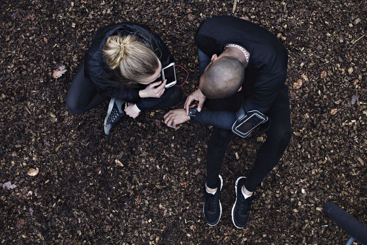 Directly above shot of couple using technologies while exercising in forest