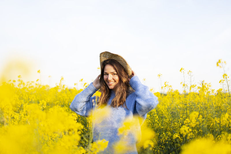 Smiling young woman with yellow flowers on field against sky