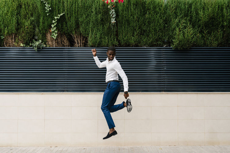 Male professional jumping on sidewalk against surrounding wall in city
