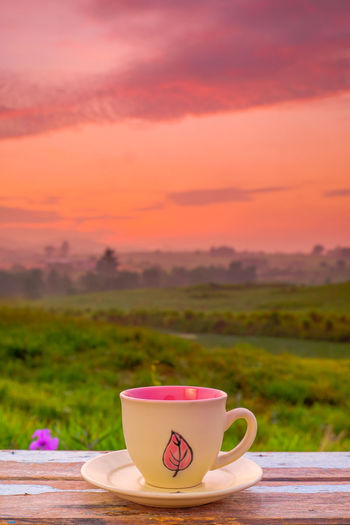 Coffee cup on table against sky during sunset