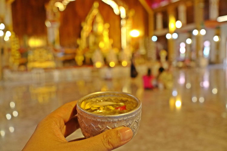Hand holding bowl of scented water to sprinkle water onto a buddha image. songkran festival.