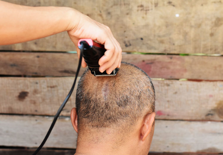 Cropped image of barber shaving head of man outdoors