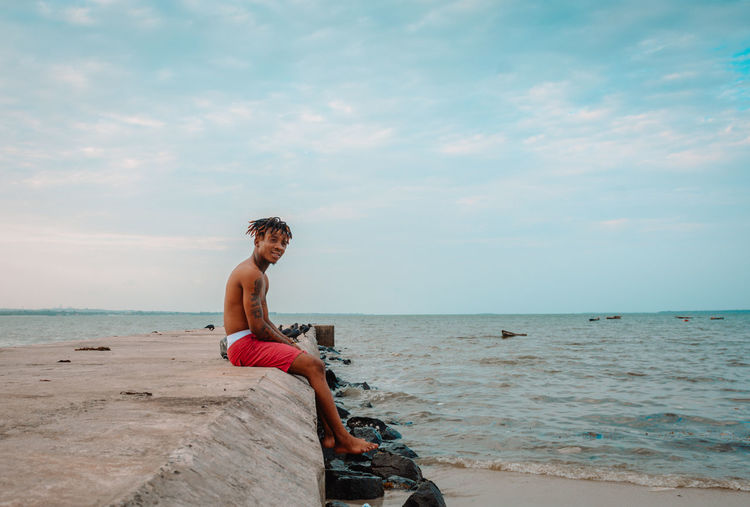 Man sitting on shore at beach against sky