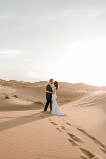Couple standing on sand dune in desert against sky
