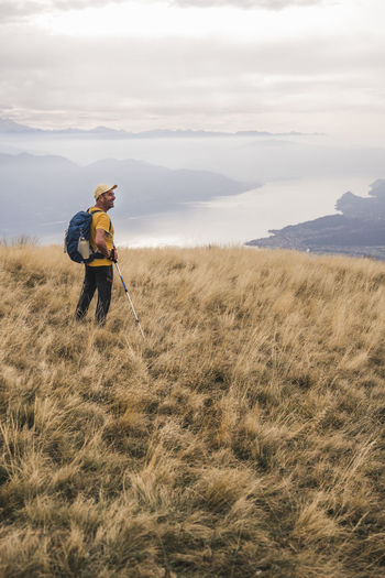 Man wearing cap standing on grass with hiking pole