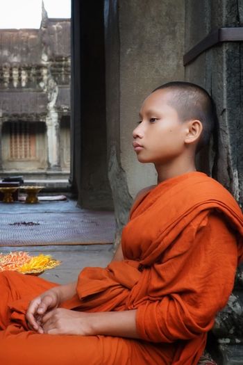 Side view of monk sitting outside temple 