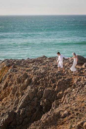 Full length of couple walking on rock by sea