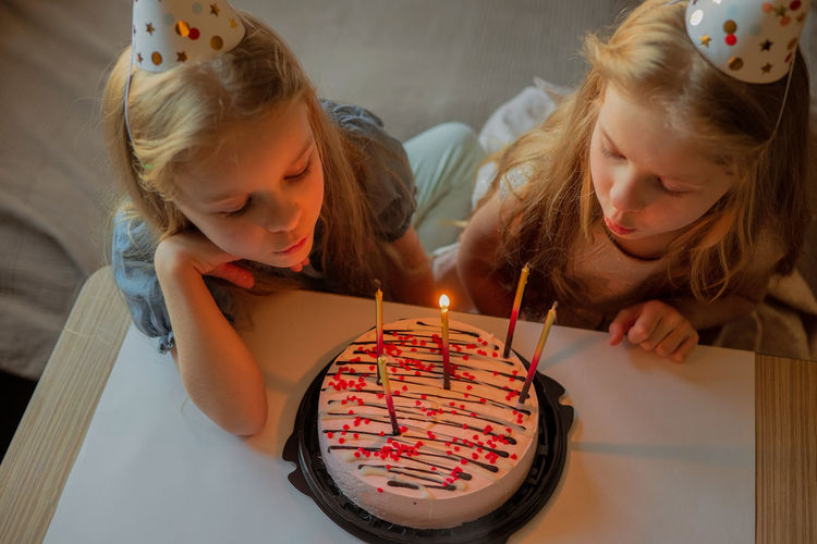 Little twin girls, children blow out candles cake birthday party at home. holiday during quarantine