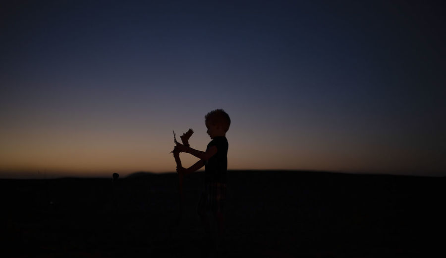 Silhouette of child standing against sky during sunset