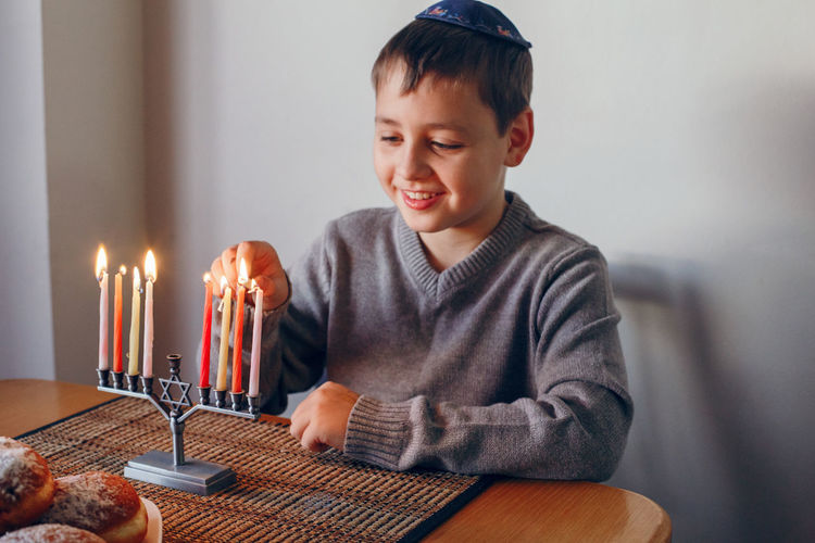 Boy in kippah lighting candles on a menorah for traditional winter jewish hanukkah holiday. 