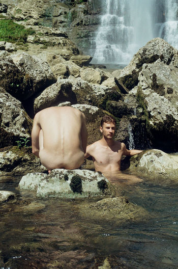 Full length of shirtless man relaxing on rock in sea