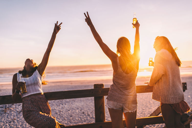 Happy female friends having drink at beach during sunset