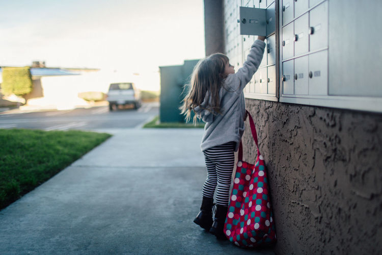 Little girl with pink bag opens door to apartment cluster mailbox