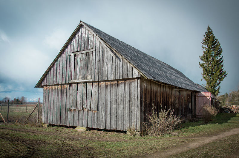 Old barn on field by building against sky